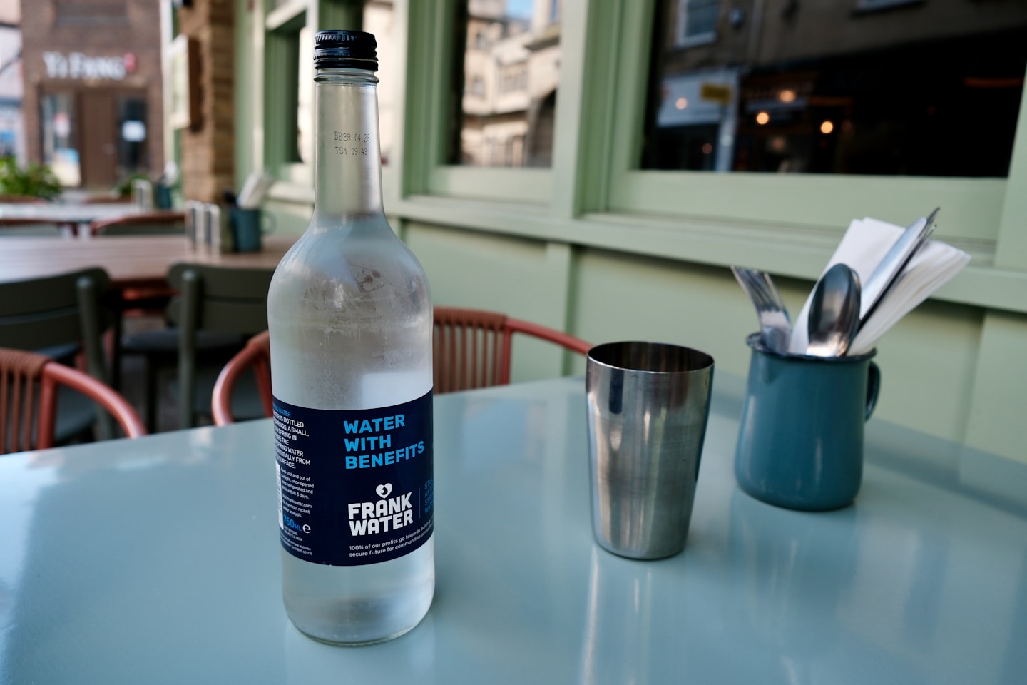 Water bottle, metal cup, and cutlery on a cafe table.
