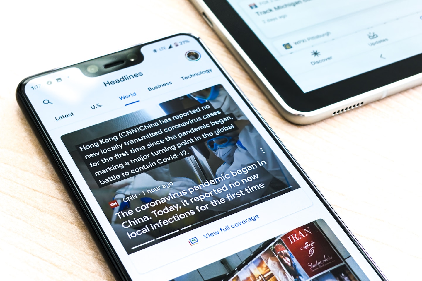A Google pixel 3XL showing Covid-19 information from the Google News app sits on a wooden table next to a Samsung Galaxy Tablet.