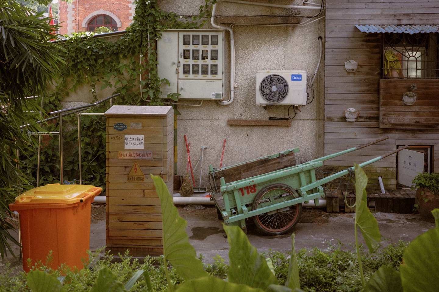 An old green cart sits next to a trash bin.
